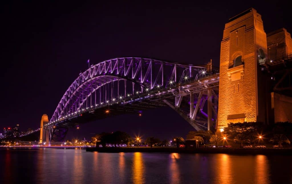 One of Sydney's lookouts at night, with the bridge lit up with colourful lights.