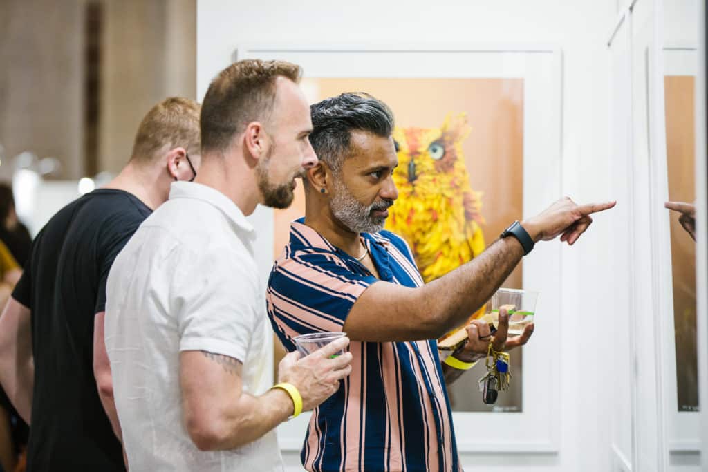 couple of men looking at and pointing at a painting on the wall at the other art fair