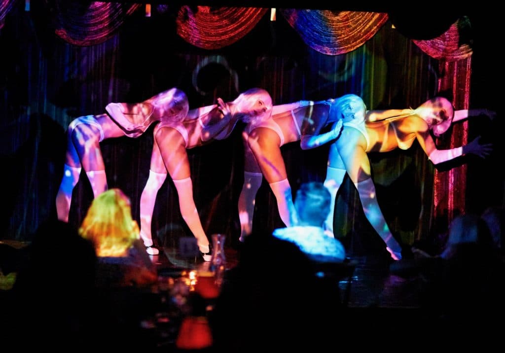 four burlesque performers lined up, coloured lighting on their bodies