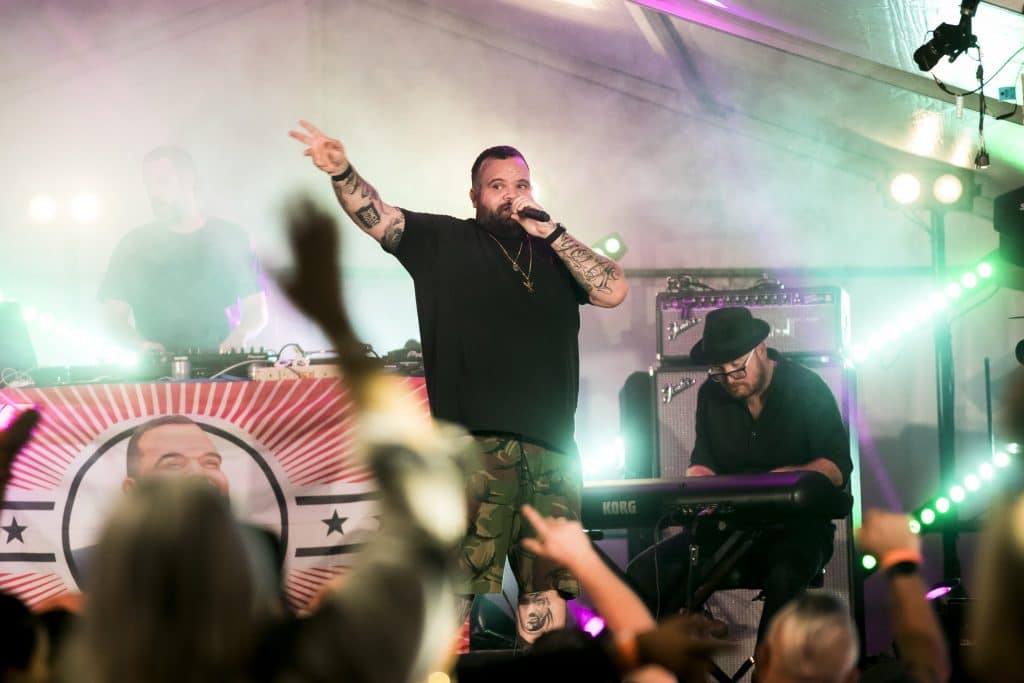 promo shot of rapper, briggs, on stage with keyboardist to his left and dj to his right