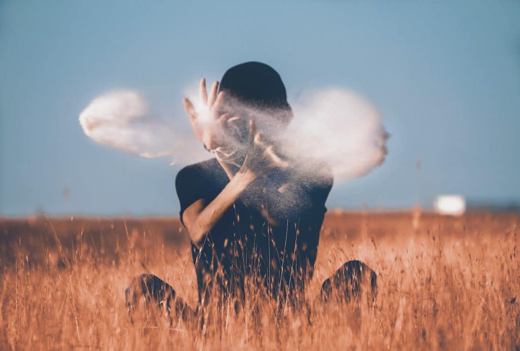 Man sitting down in a field throwing white powder in the air as if doing a magic trick