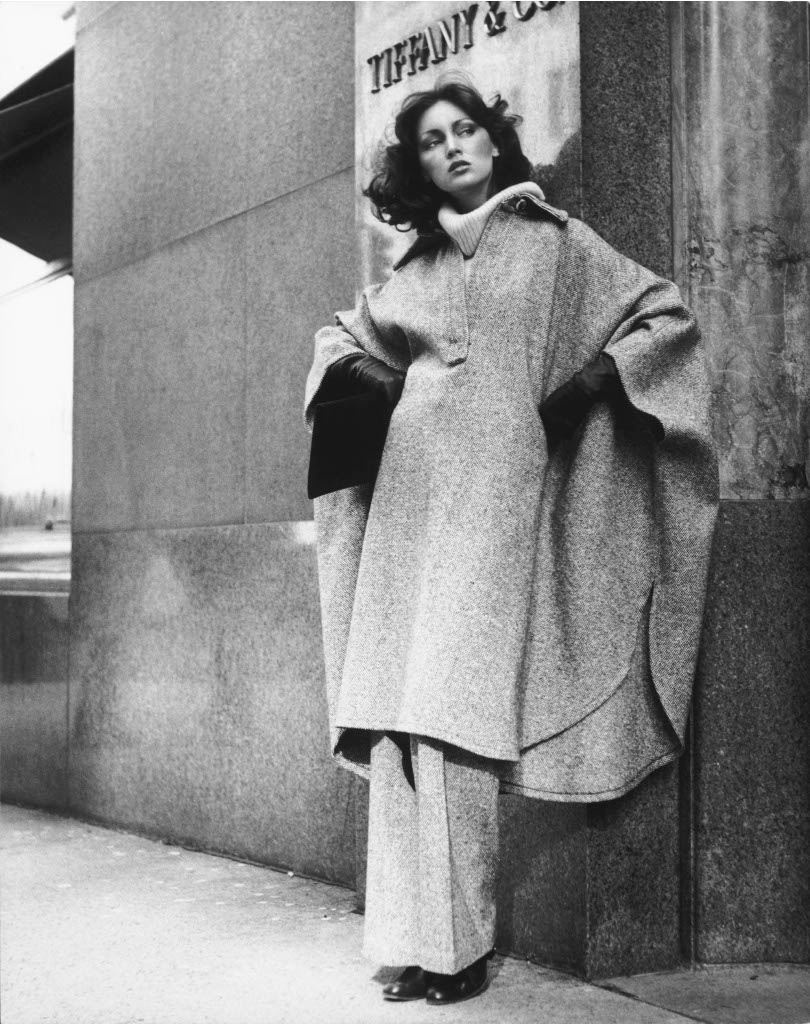 Carla Zampatti photographed on sidewalk wearing poncho/coat, black and white, as part of retrospective exhibition
