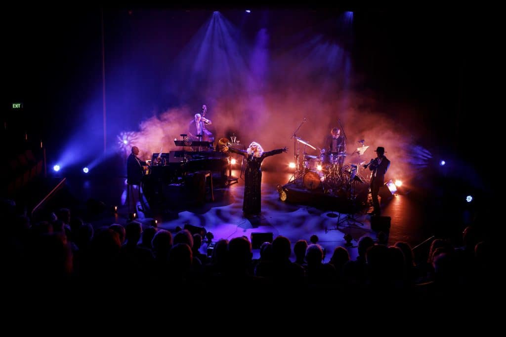 stage show with band, singer arms wide open and dark, moody lighting