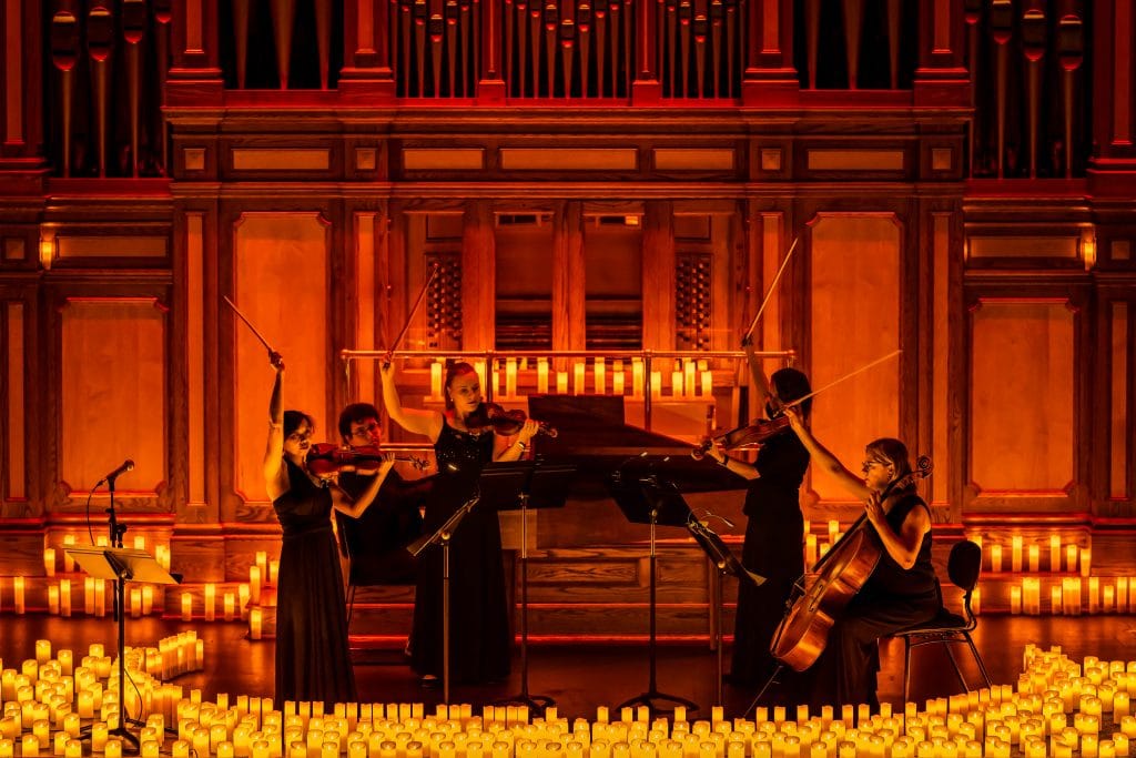 quartet and pianist on stage playing instruments surrounded by candles