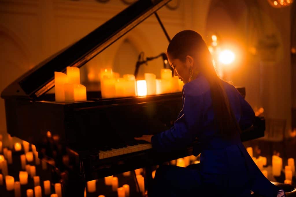 woman pianist at piano surrounded by candles, as seen from behind