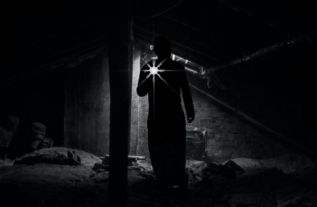 silhouette of person holding a flashlight in what looks like a basement