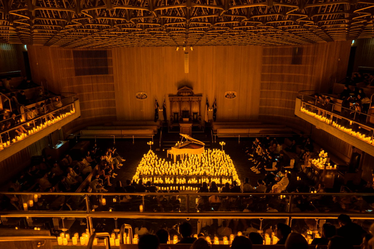 A shot taken from the balcony inside the Sydney Masonic Centre looking down on a stage lit by hundreds of candles and a pianist performing in the centre of it.