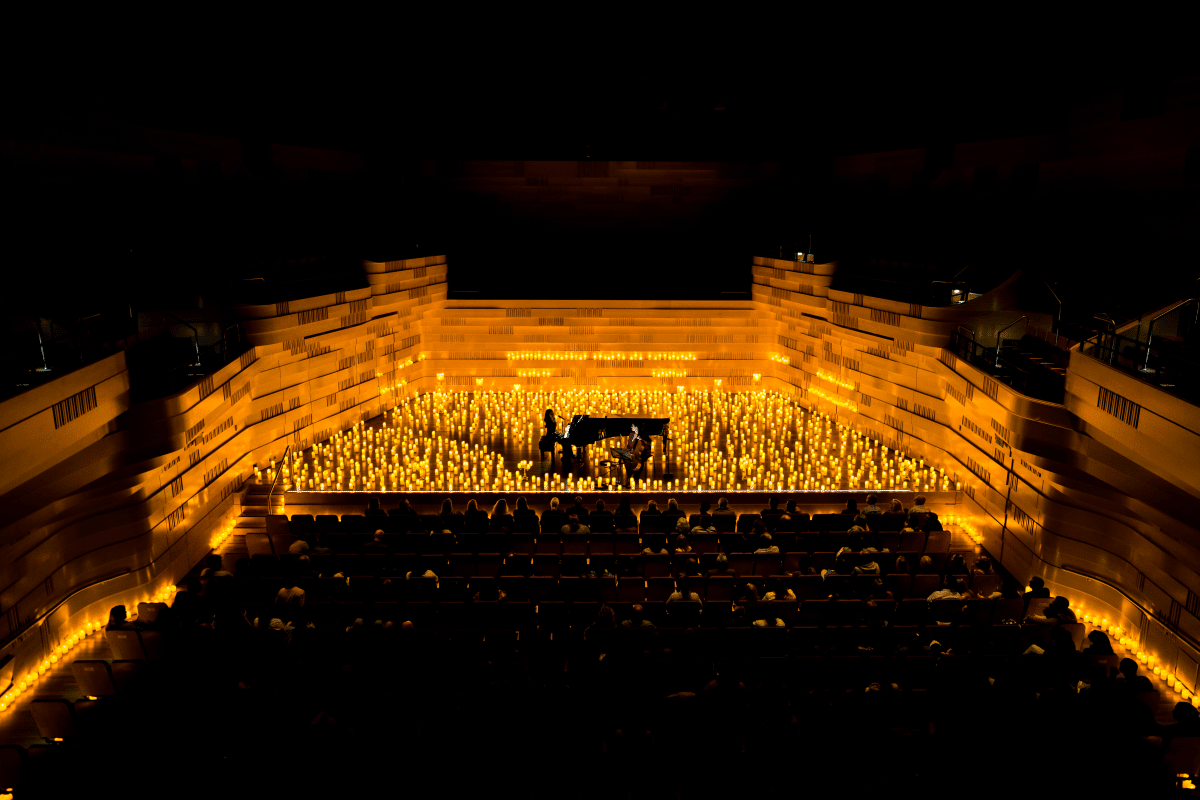 A wide shot of a stage covered in almost entirely by candles with a pianist performing in the centre of it all.