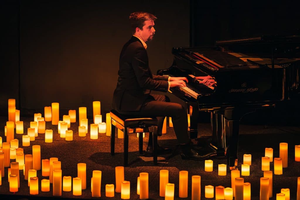 side view of pianist surrounded by candles