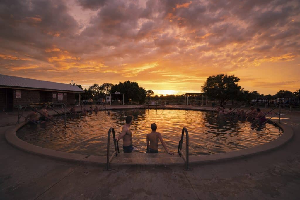 Two guests descend into hot springs as the sun sets in the background.