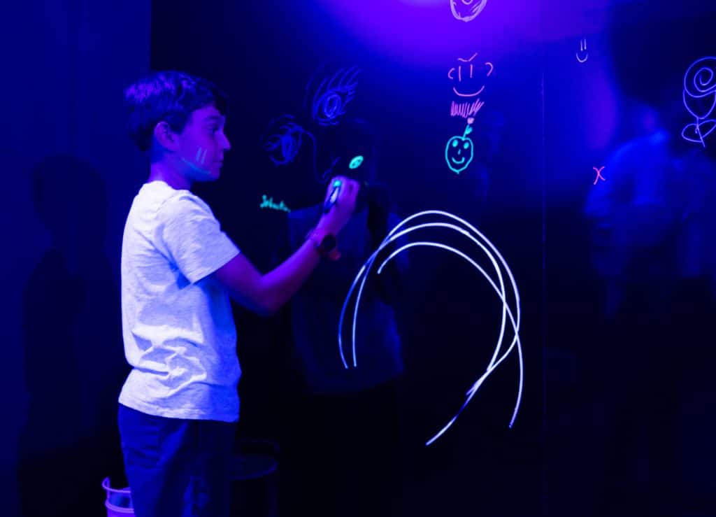 young boy writing on wall with neon paint at chaos lab experience in sydney