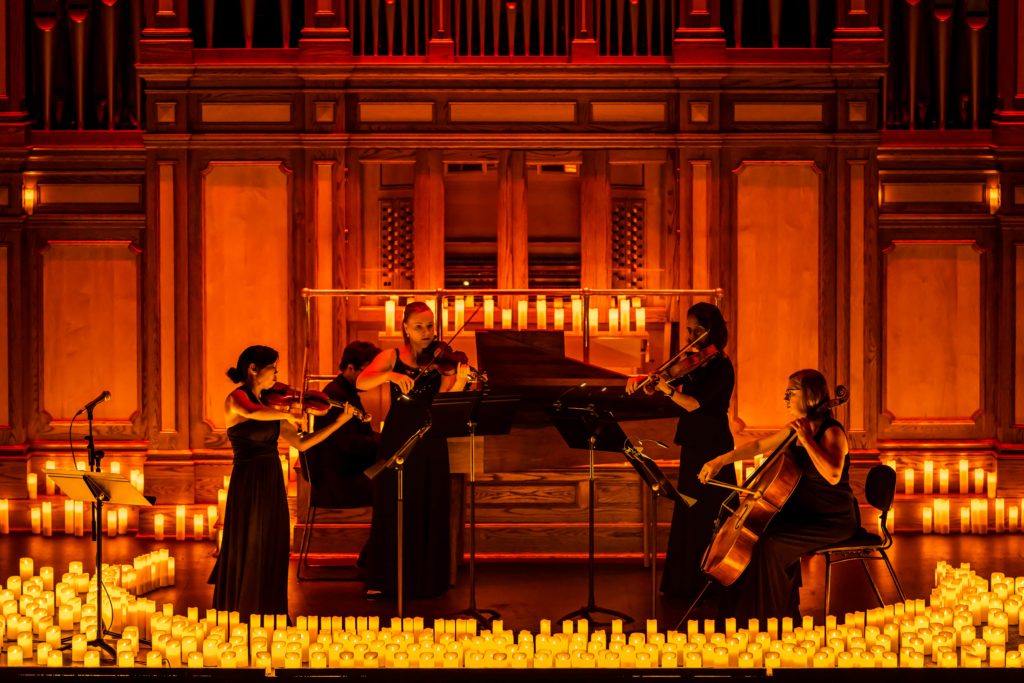 string quartet and pianist on stage performing surrounded by candles