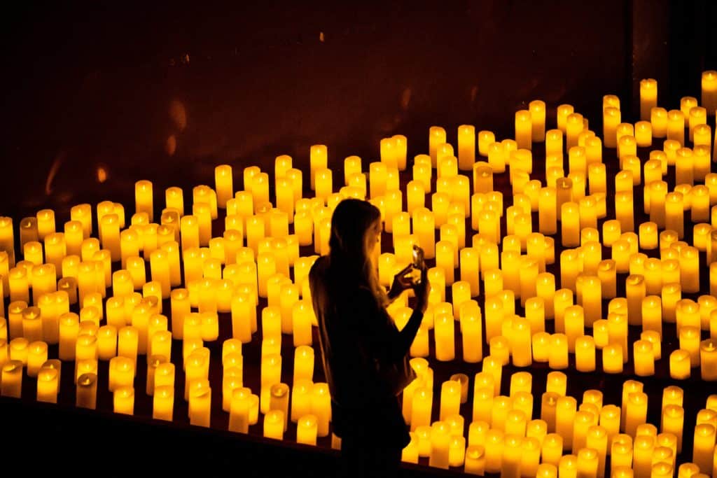 silhouette of a woman taking a photo of hundreds of candles on her phone at candlelight