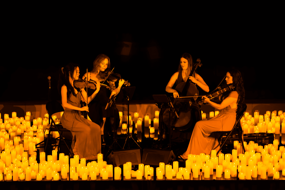 A string quartet sitting and performing on a stage surrounded by candles.