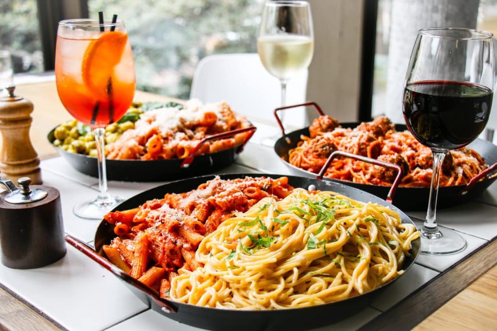 bowls of pasta and glasses of wine placed on a table