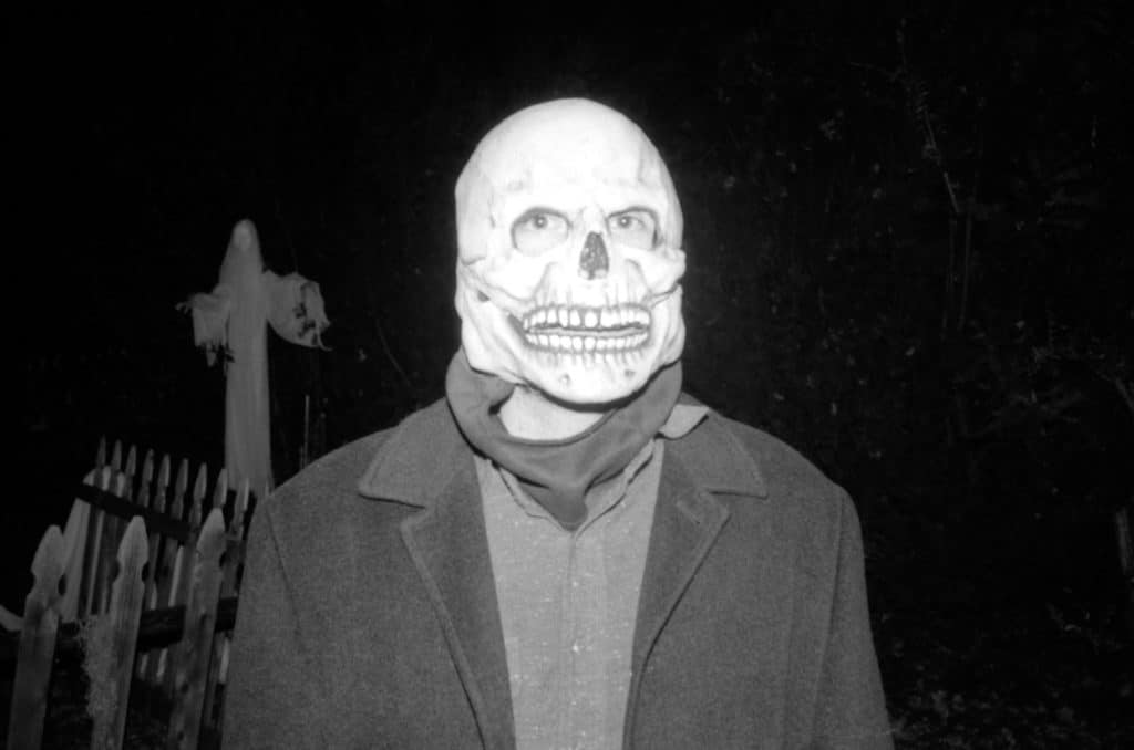 person dressed in trench with skull mask on head, black and white
