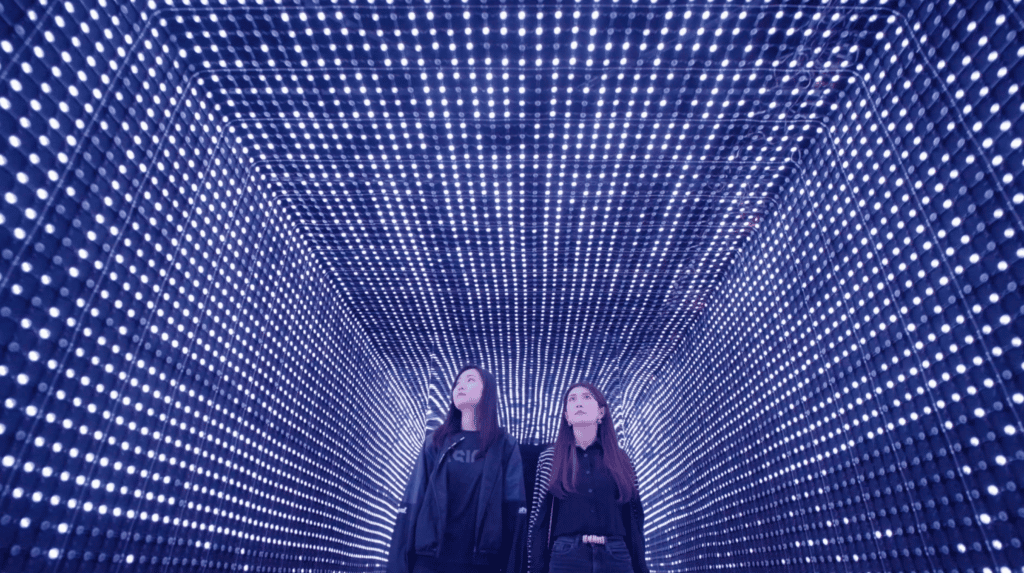 two women walking towards the camera through a led light installation at enlightenment