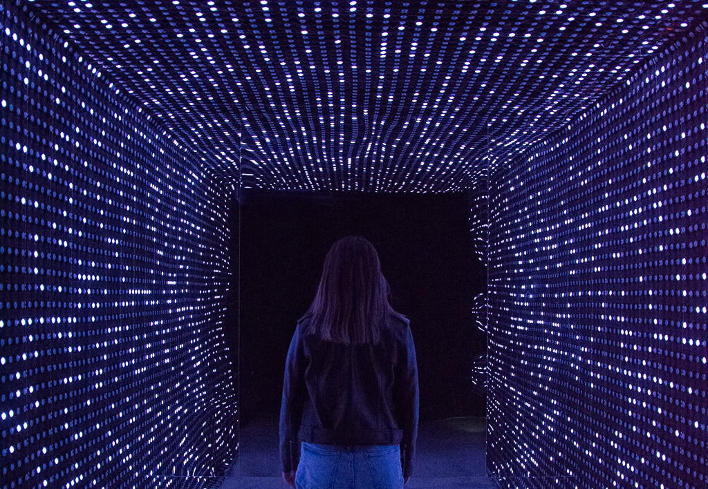 young woman walking through led light installation towards black hole at enlightenment
