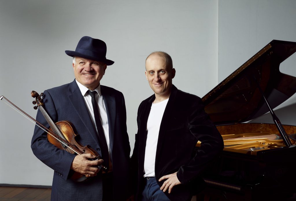 promo image of george washingmachine holding his violin with simon tedeschi standing in front of an open grand piano