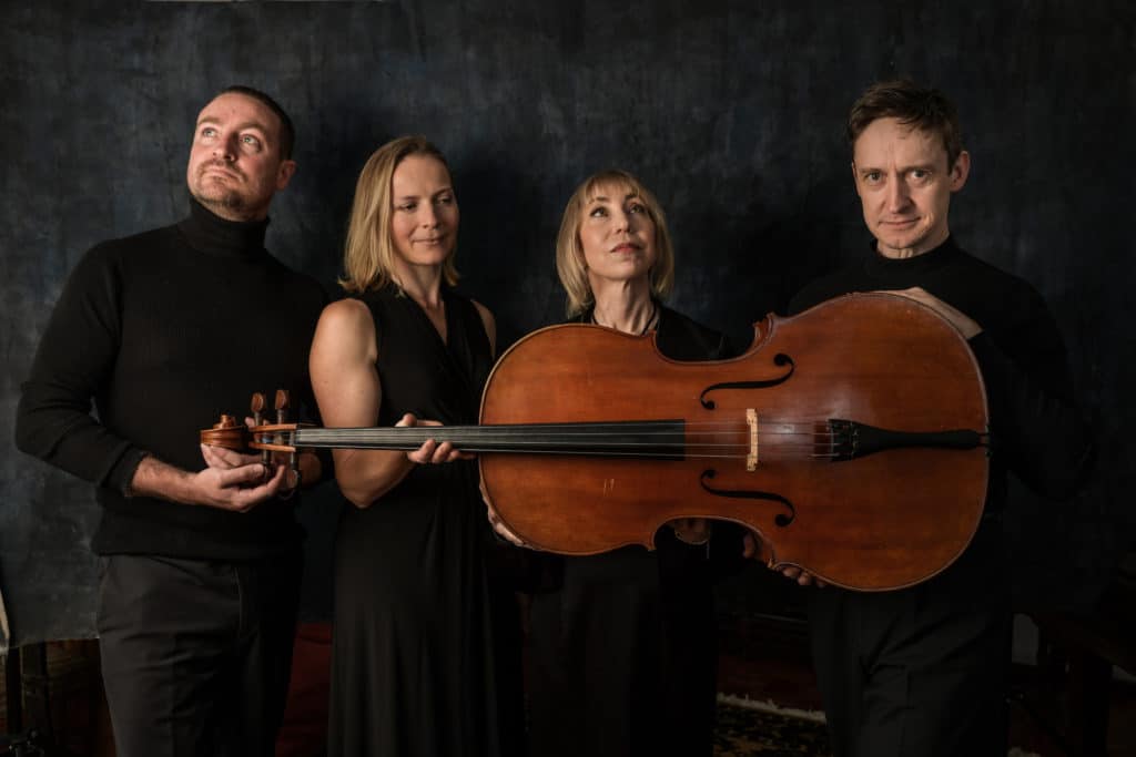 dressed in black, the pheonix collective string quartet posing with a cello held across their chests