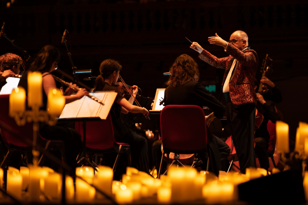 A man conducting an orchestra with candles surrounding them.