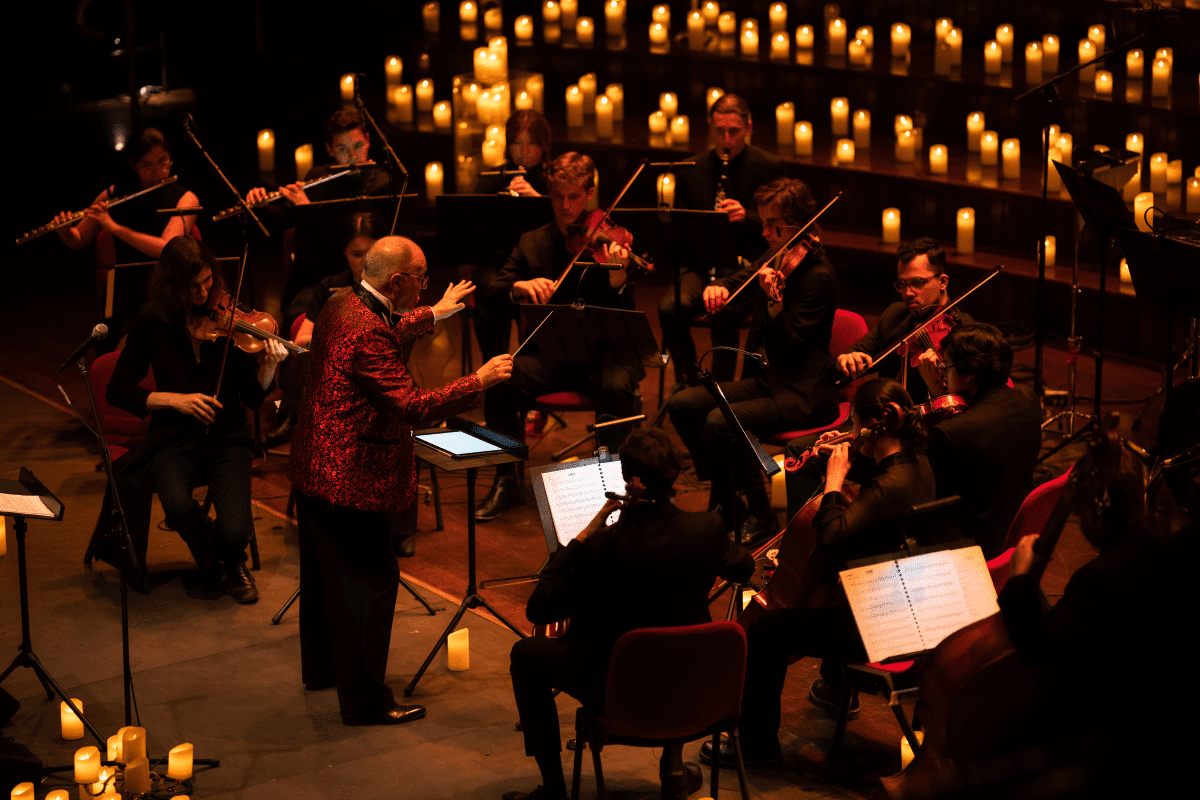 A man conducting an orchestra with a sea of candles behind them.