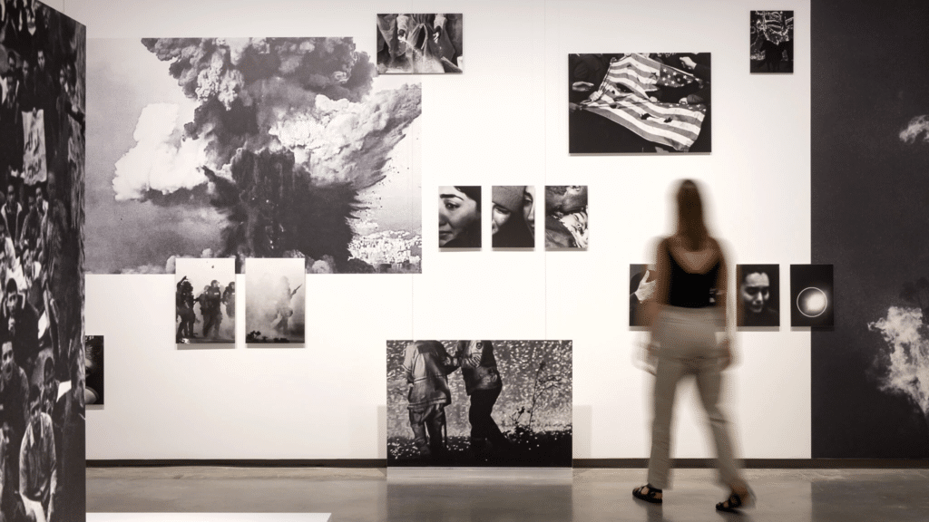 A woman stands in front of a wall of photographs at an art exhibition