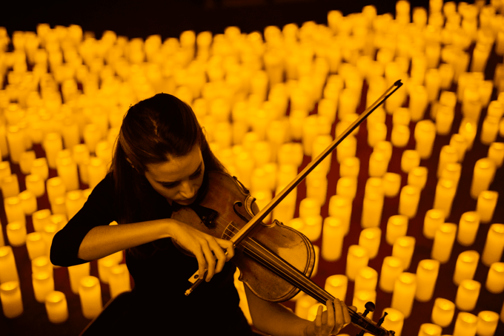 A violinist playing while surrounded by hundreds of candles 