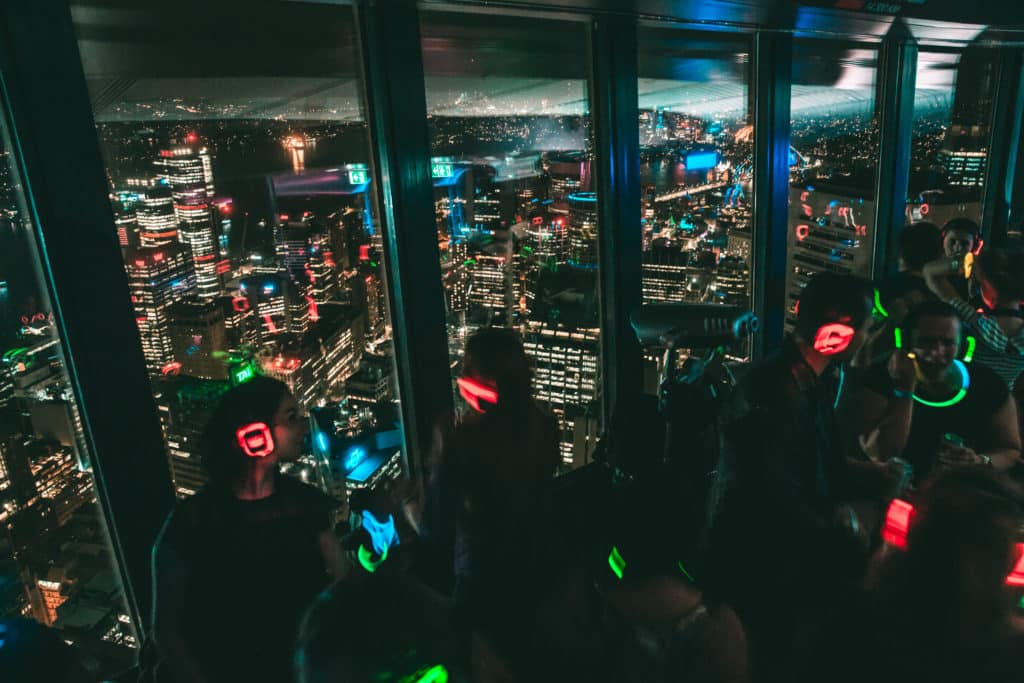 people looking over a city from an observation deck wearing lit up headphones