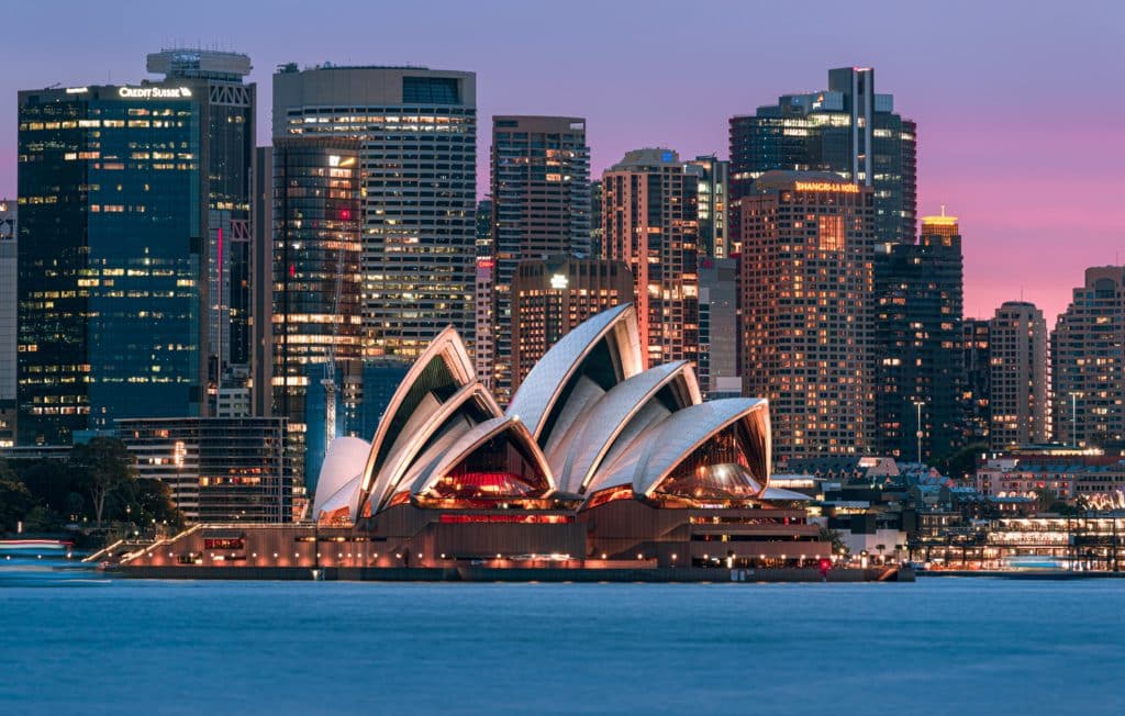 sydney opera house at dusk with buildings and offices in the backdrop
