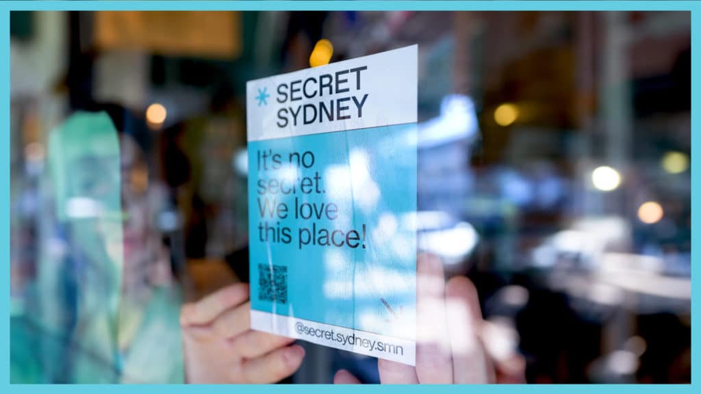 A Secret Sydney sticker being placed on a window